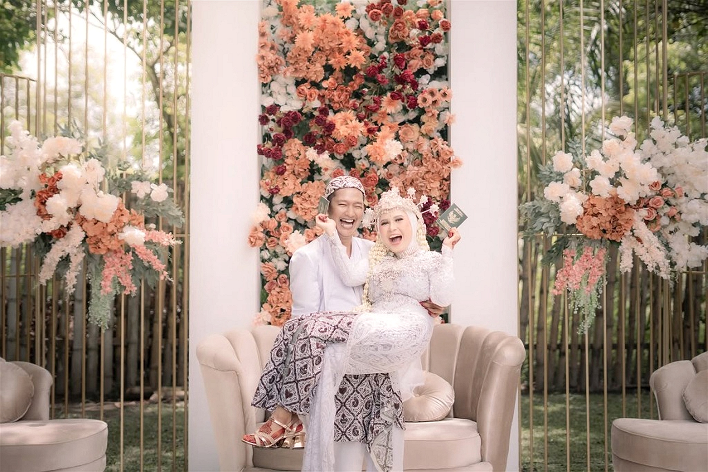 Momen bahagia kedua mempelai memperlihatkan buku nikah di pelaminan taman